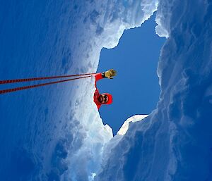 Image of a field training officer (FTO) standing above a crevasse in the ice looking down at a glaciologist.