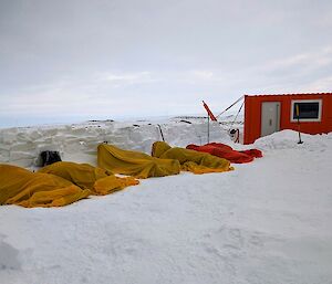 image of five expeditioners asleep in survival bivy bags for training. An orange shelter is seen in the mid-ground.