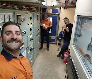 A man in orange and two other fellows with electrical equipment