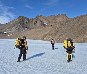 Three people walk across snow, heading for a rocky hill