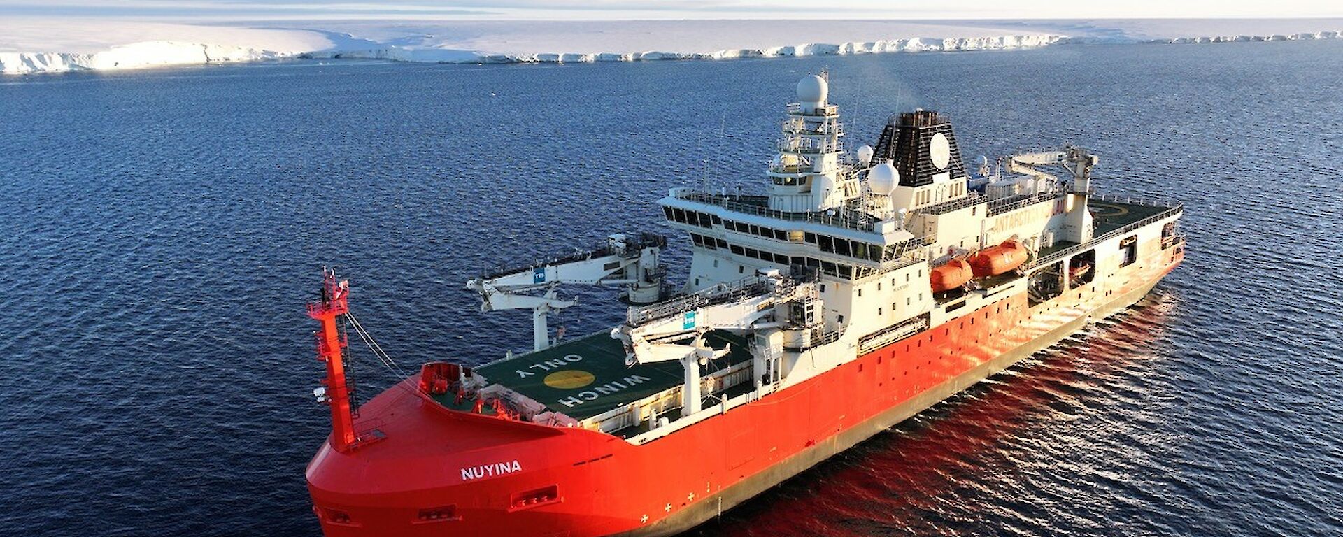 A big red and white ship in front of a jagged icy coastline