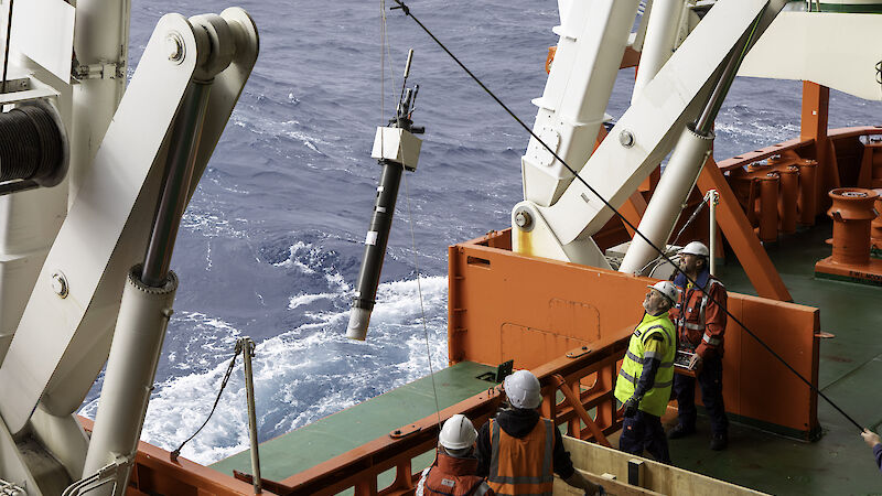 A long dark cylinder is put into the ocean from a ship.