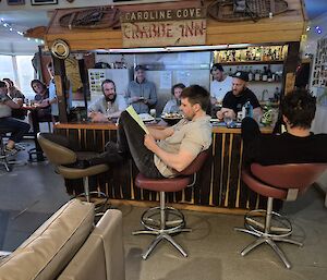 A man sits on a bar stool reading from a notebook