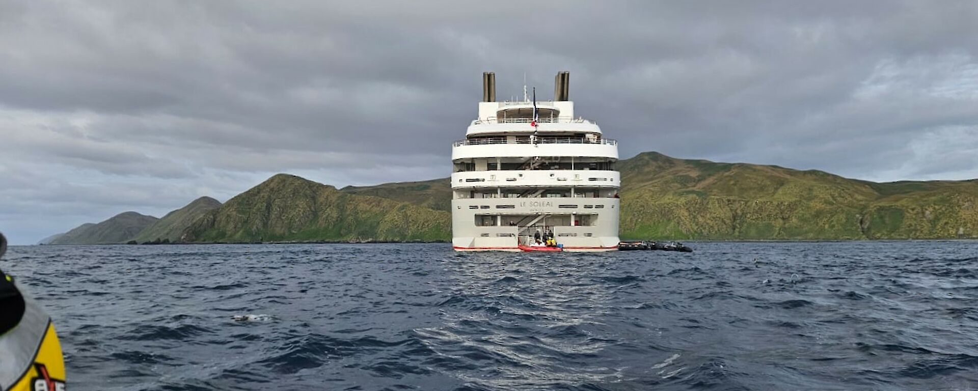 Photo taken from small boat as it approached stern of large vessel. Mountains of island in the background.