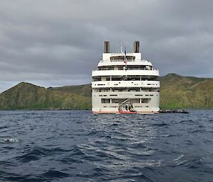 Photo taken from small boat as it approached stern of large vessel. Mountains of island in the background.