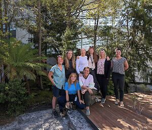 A group of eight women, five standing and two kneeling, smile to camera.