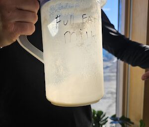 A plastic jug, with a tiny bit of milk in the bottom, with the words Full Fat Milk on it and signs