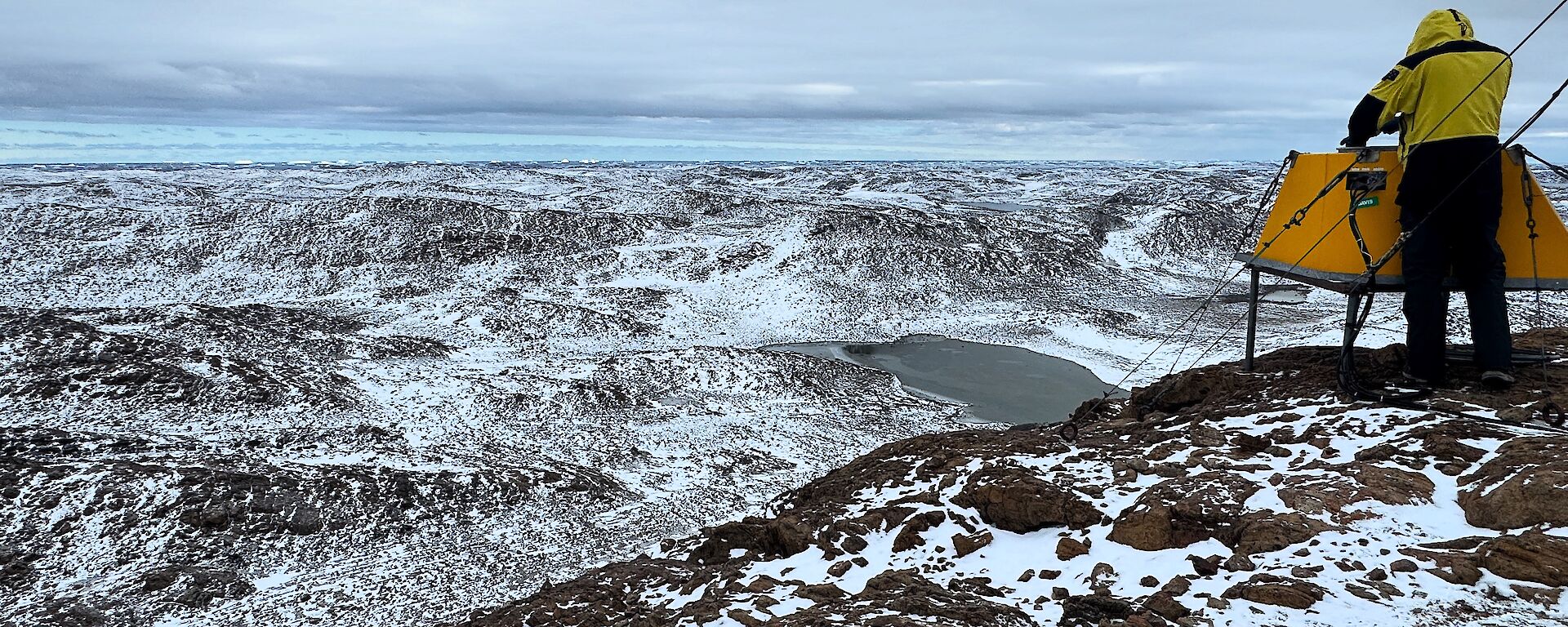 A man overlooks a snow-covered valley from a rocky outcrop
