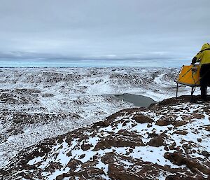 A man overlooks a snow-covered valley from a rocky outcrop