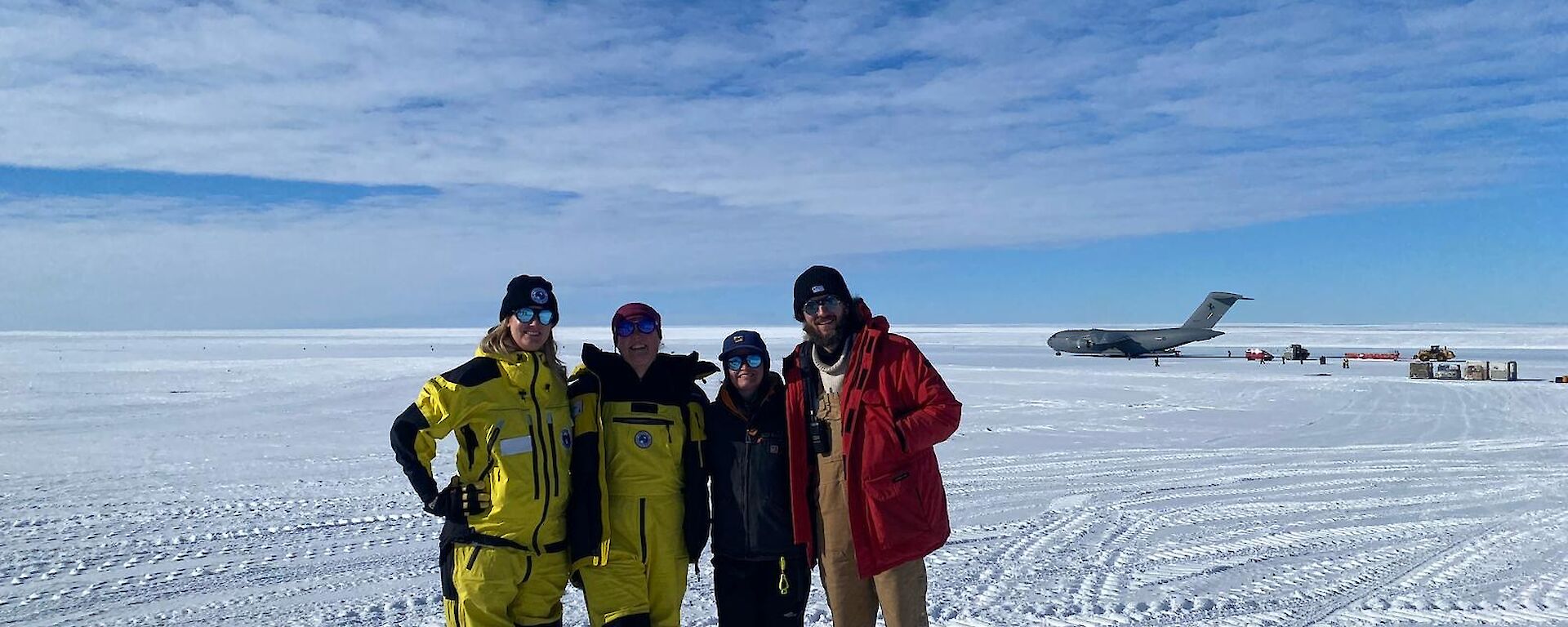 Four people stand together on the ice runway with the C17 in the background