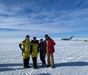 Four people stand together on the ice runway with the C17 in the background