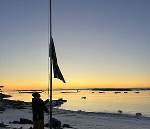 A sole figure raises a flag on a flagpole at sunrise