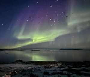 Green shimmering lights in the starry sky over a still body of water