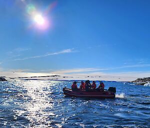 5 expeditioners in a small inflatable rigid hull boat with small ice bergs in the background as they explore the ocean
