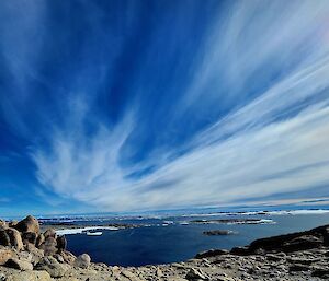 View of the bright blue ocean, whispy white clouds and distant ice bergs taken from a rock outcrop on the top of Reeves Hill