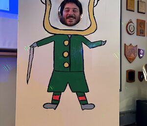 A man sticking his face into a cardboard drawing of a leprachaun, with the face cut out