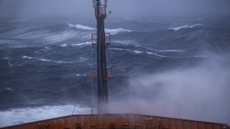 The bow of a big red ship in huge seas