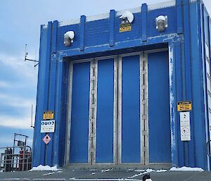 A penguin standing in front of a large, blue shed in Antarctica