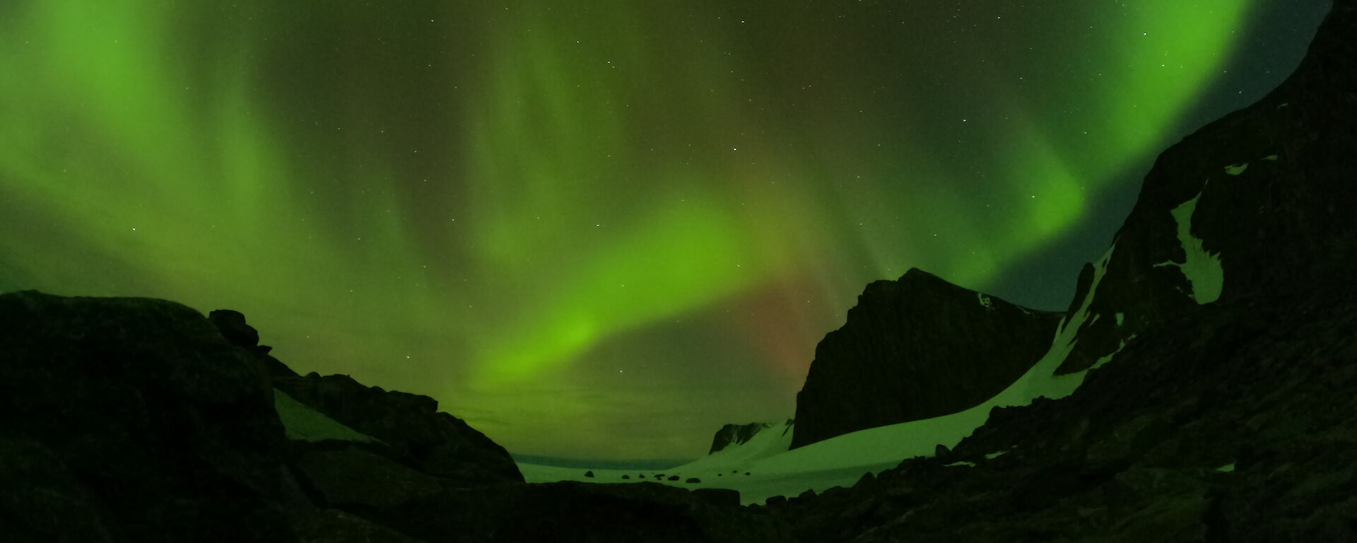 A green aurora lighting up the night sky over Mawson's rocky mountains