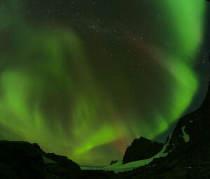 A green aurora lighting up the night sky over Mawson's rocky mountains
