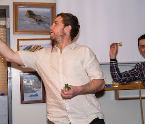 One man throws a dart while another prepares to throw one.