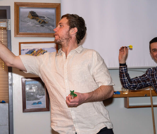 One man throws a dart while another prepares to throw one.