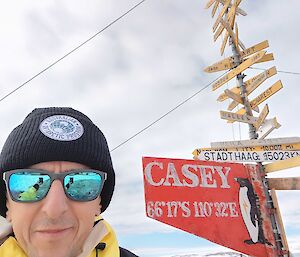 A man in a beanie and sunglasses in front of the Casey station signpost