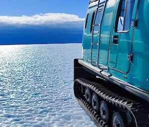 A teal blue hagglund parked on pock-marked sea ice