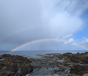 Two rainbows over the ocean with kelp-covered rocks in the foreground