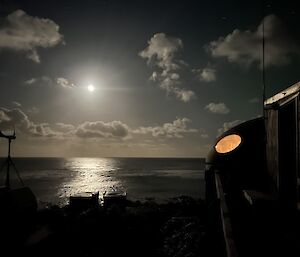 The moon rises over the ocean with some field huts in the foreground