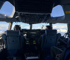 A view from the cockpit of the C17 standing behind the two pilots who are flying the plane and looking out through the windscreen.