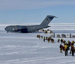 A group of Antarctic expeditioners step off the C17 planeand walk in a group away from the plane.