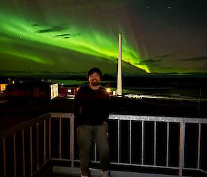 An expeditioner at Mawson station, standing underneath an aurora