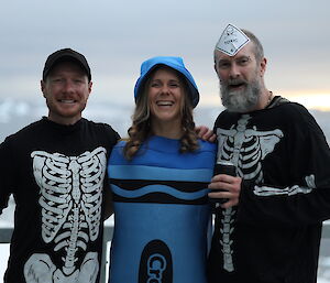 Two men in skeleton shirts, stand either side of a woman in a blue outfit and hat