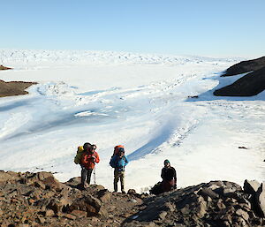 Three people walking down a rocky hill before a sweeping plain of white