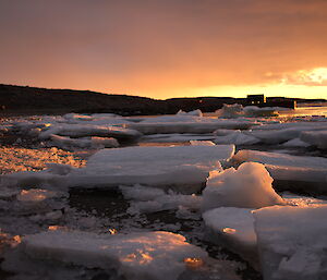 Sunset in the background and large blocks of ice on the ground in the foreground