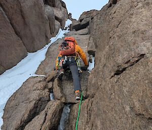 A person using ropes to climb up a cliff with snow to the left