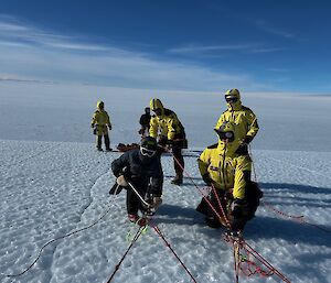 Five people in yellow hold onto rope harnesses as they walk up a snowy slope