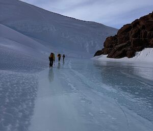 Three people in the distance, walking on a frozen blue river