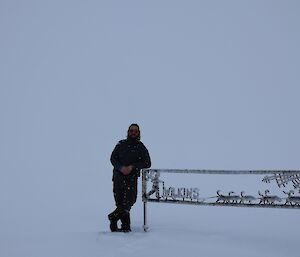 An expeditioner leaning against the Wilkins sign on a sea of ice