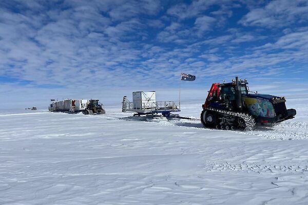 A tractor-train hauling sleds of shipping containers across snow
