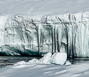 An iceberg with long dangling shards of ice set against the water
