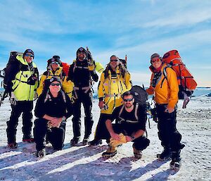 Seven expeditioners with their field packs and other equipment on the ice with water in the background