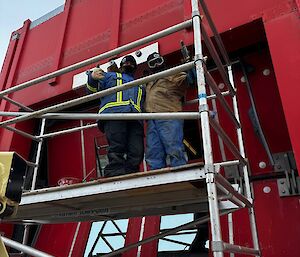 Two people on scaffolding against the Red Shed