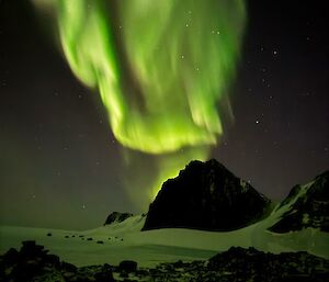 A plume of green light behind a dark hill at night