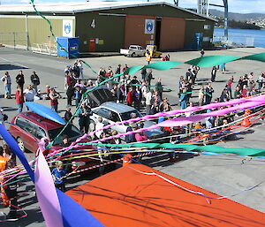 Looking down on the wharf from the ship, with streamers and cars and people standing around.