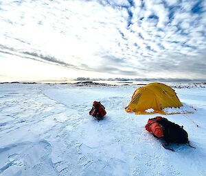 A yellow tent on the ice under dappled cloud