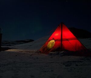 A red tent on the ice at night time with a light inside