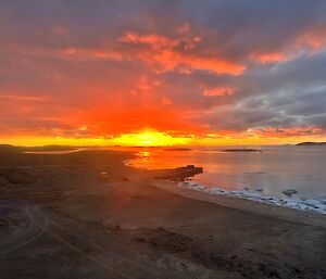 An orange sunset over a brown rocky landscape with water and ice in the background