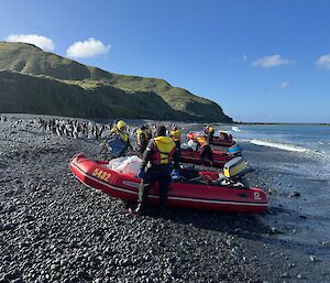 Three red inflatable boats and crew pulled up onto rocky beach